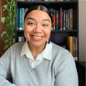 Smiling picture of a woman wearing a grey sweater in front of a bookcase.